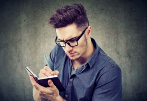 A man with glasses writes something in his notebook with concentration.